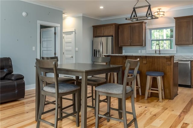 kitchen featuring a breakfast bar area, ornamental molding, stainless steel fridge, light stone countertops, and light hardwood / wood-style floors