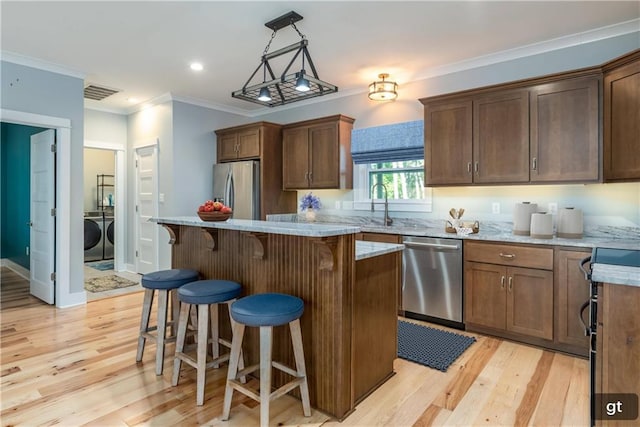 kitchen with a center island, decorative light fixtures, appliances with stainless steel finishes, washing machine and dryer, and light hardwood / wood-style floors