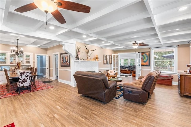 living area with coffered ceiling, light wood finished floors, beam ceiling, and ceiling fan with notable chandelier