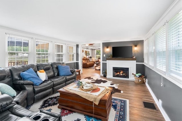 living room with visible vents, baseboards, a glass covered fireplace, ornamental molding, and wood finished floors
