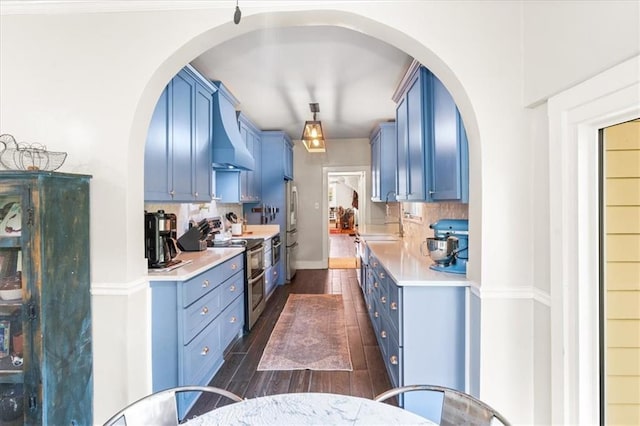 kitchen featuring double oven range, blue cabinetry, light countertops, and wall chimney exhaust hood
