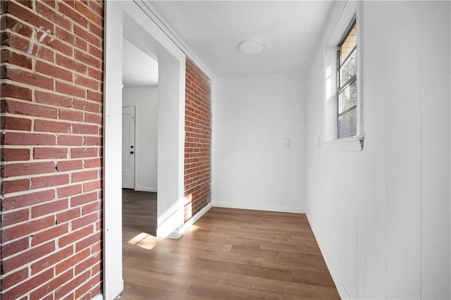 hall with wood-type flooring and brick wall