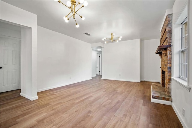 unfurnished living room with an inviting chandelier, a fireplace, light wood-type flooring, and a healthy amount of sunlight