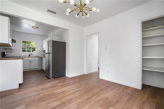 kitchen with stainless steel refrigerator, light wood-type flooring, and white cabinetry