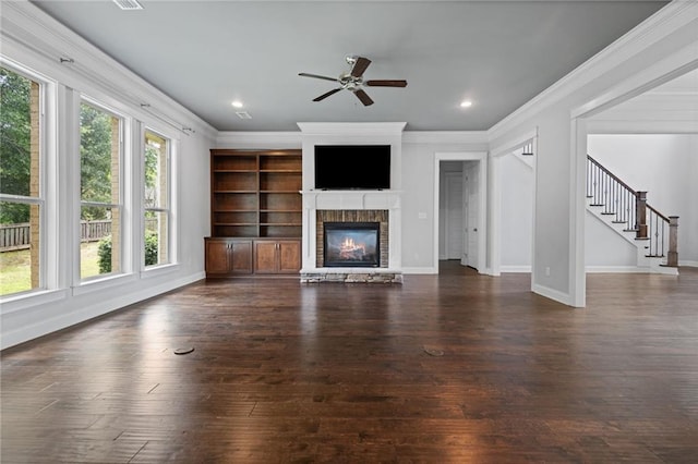 unfurnished living room with ornamental molding, ceiling fan, dark wood-type flooring, and a stone fireplace