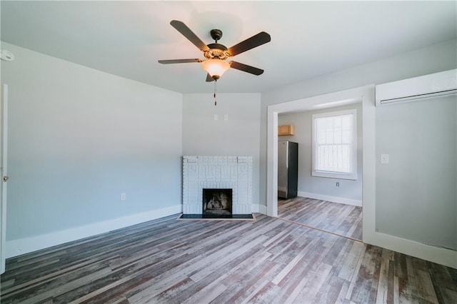 unfurnished living room featuring a wall unit AC, a brick fireplace, hardwood / wood-style floors, and ceiling fan