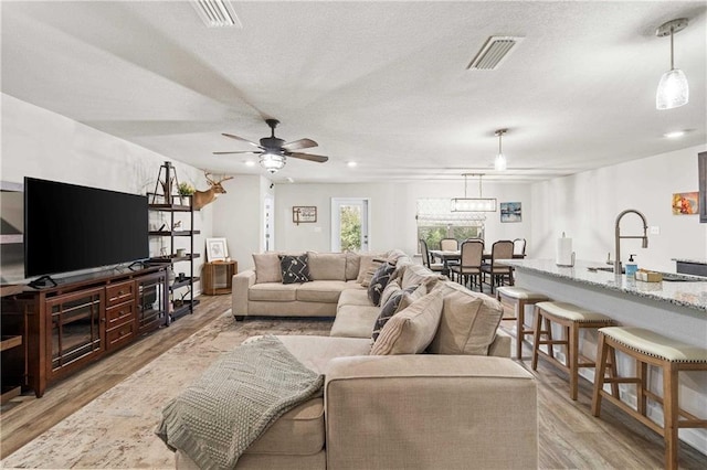 living room featuring a textured ceiling, ceiling fan, sink, and light hardwood / wood-style flooring