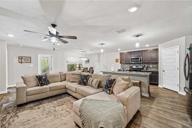 living room featuring ceiling fan, a textured ceiling, and dark wood-type flooring