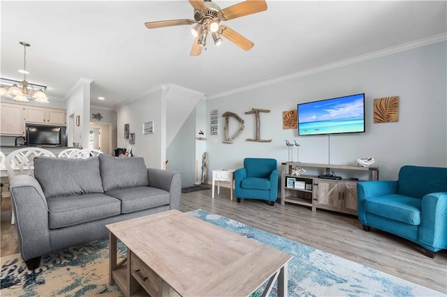 living room with wood-type flooring, ceiling fan with notable chandelier, and crown molding