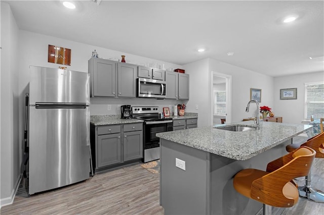 kitchen featuring gray cabinetry, sink, stainless steel appliances, an island with sink, and a breakfast bar area