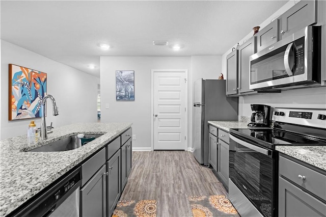 kitchen with appliances with stainless steel finishes, light wood-type flooring, light stone counters, sink, and gray cabinets