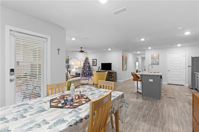 dining space with light hardwood / wood-style floors, ceiling fan, and sink