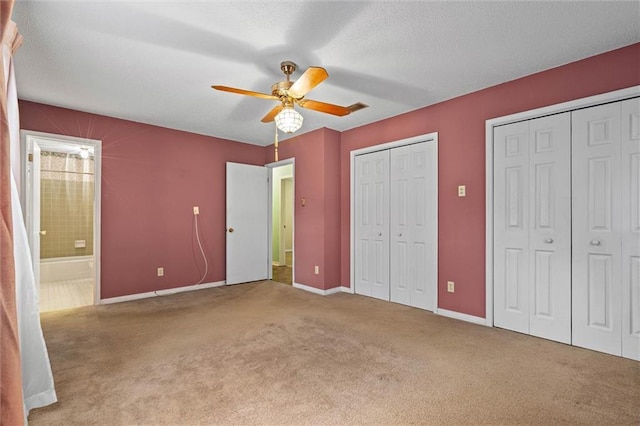 unfurnished bedroom with carpet flooring, ensuite bath, two closets, and baseboards