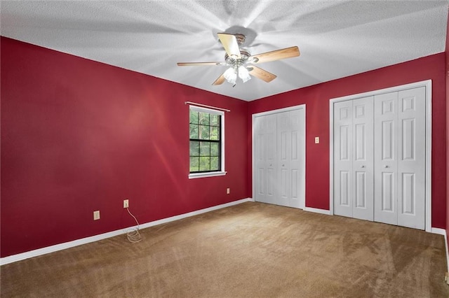 unfurnished bedroom with carpet, two closets, baseboards, and a ceiling fan