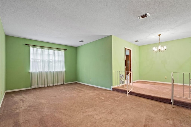 unfurnished room featuring a chandelier, a textured ceiling, carpet flooring, and visible vents