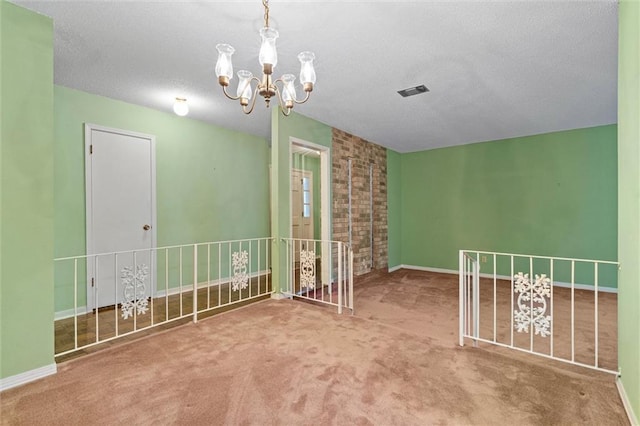 carpeted spare room with a textured ceiling, a notable chandelier, baseboards, and visible vents