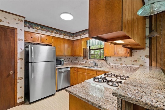 kitchen with a sink, brown cabinetry, stainless steel appliances, and wallpapered walls