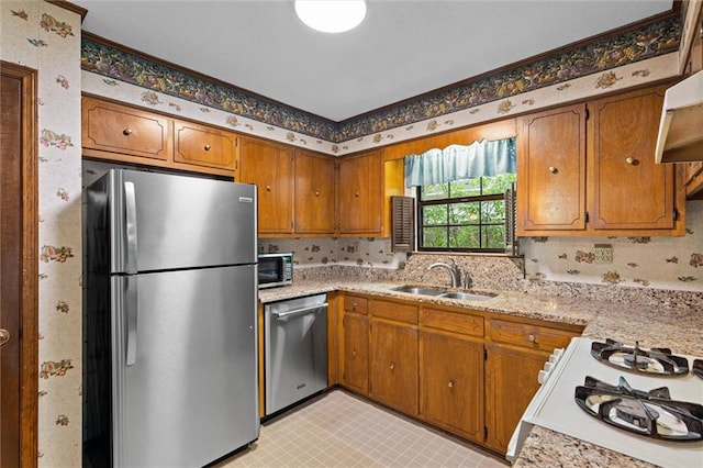 kitchen with brown cabinetry, stainless steel appliances, wallpapered walls, and a sink