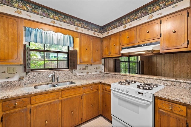kitchen featuring brown cabinets, under cabinet range hood, a sink, and white gas range oven