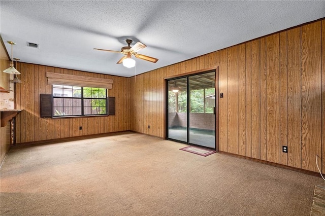 spare room featuring ceiling fan, wood walls, a textured ceiling, and visible vents