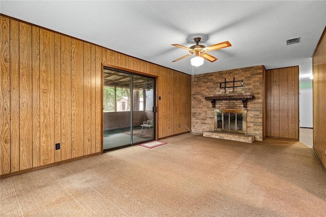 unfurnished living room with carpet flooring, a ceiling fan, a fireplace, visible vents, and wooden walls