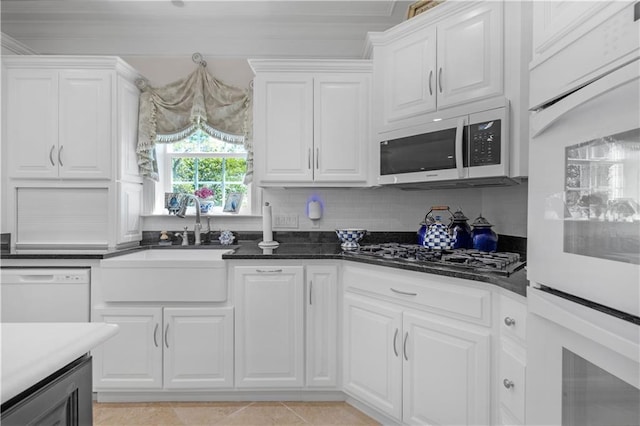 kitchen featuring a sink, white cabinetry, tasteful backsplash, light tile patterned floors, and white appliances