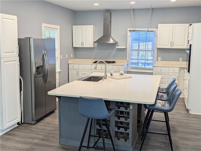 kitchen featuring wall chimney range hood, a breakfast bar area, appliances with stainless steel finishes, wood finished floors, and white cabinets