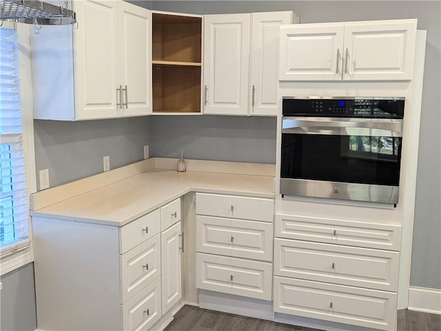 kitchen with stainless steel oven, dark wood finished floors, light countertops, and white cabinetry