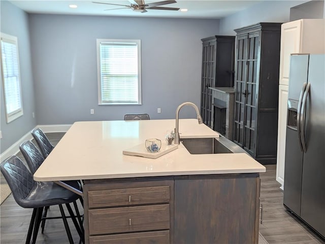 kitchen with wood finished floors, baseboards, a sink, light countertops, and stainless steel refrigerator with ice dispenser