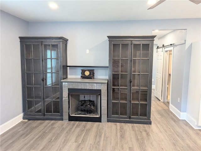 unfurnished living room featuring a barn door, baseboards, wood finished floors, and a fireplace