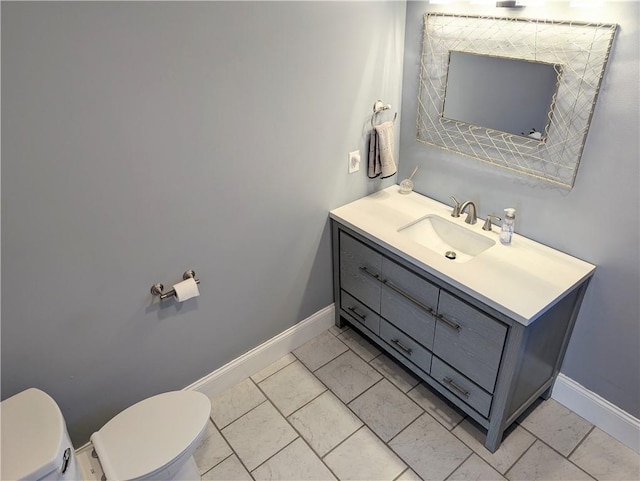 bathroom with vanity, toilet, baseboards, and marble finish floor