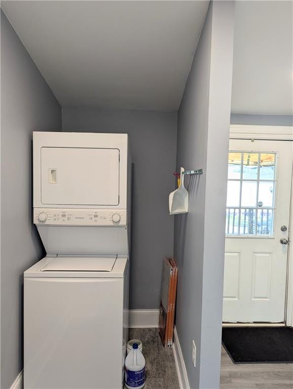 washroom featuring laundry area, stacked washer / dryer, wood finished floors, and baseboards