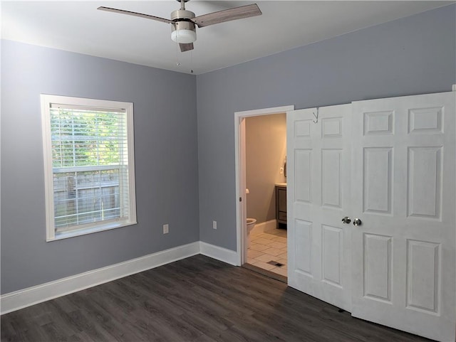 unfurnished bedroom featuring ceiling fan, baseboards, dark wood-style floors, and ensuite bathroom