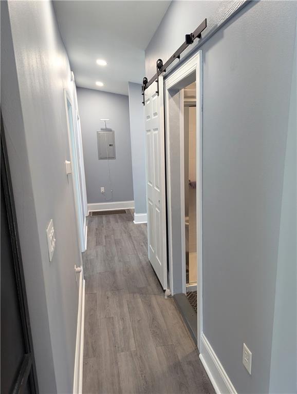 corridor with recessed lighting, a barn door, baseboards, and wood finished floors