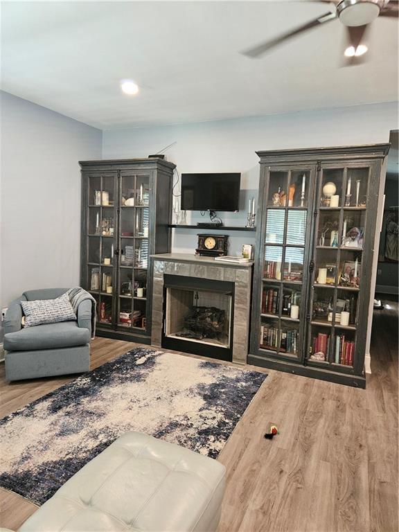 living room with a tile fireplace, ceiling fan, and wood finished floors