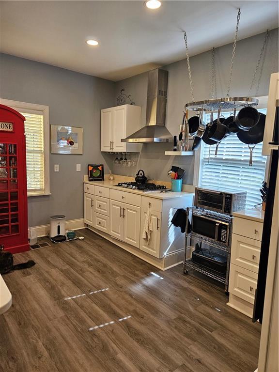 kitchen featuring stainless steel gas cooktop, dark wood-type flooring, light countertops, white cabinets, and wall chimney range hood