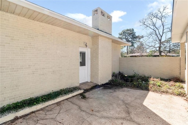 entrance to property with brick siding, fence, a chimney, and a patio