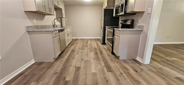 kitchen with white cabinetry, stainless steel appliances, sink, light stone counters, and light hardwood / wood-style floors