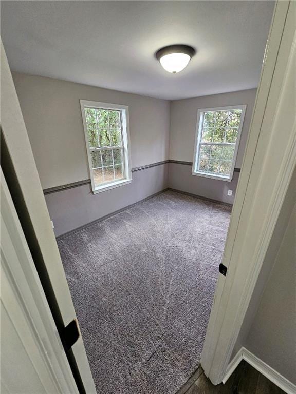 spare room with a wealth of natural light and dark carpet