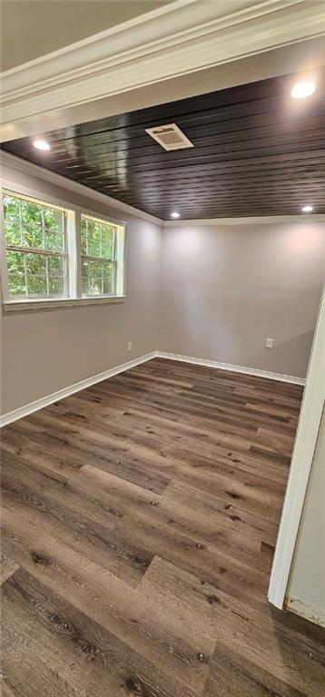 empty room with ornamental molding, dark hardwood / wood-style flooring, and wooden ceiling