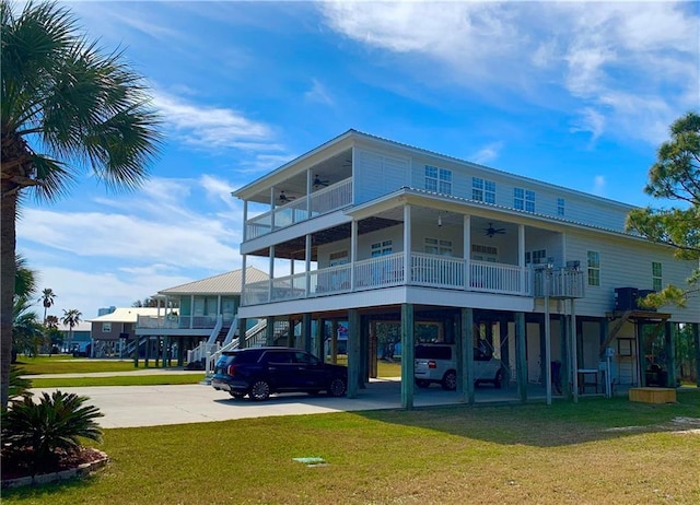 back of house featuring a ceiling fan, driveway, a yard, stairway, and a carport