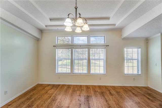 unfurnished dining area with an inviting chandelier, a textured ceiling, a raised ceiling, and wood finished floors