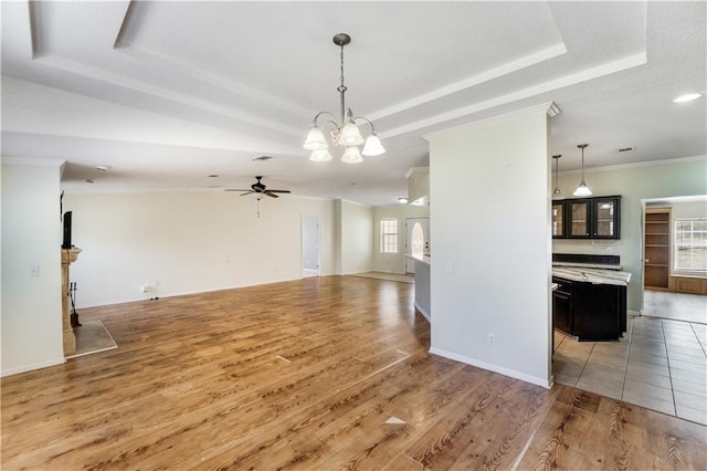 interior space featuring light wood-style flooring, ceiling fan with notable chandelier, baseboards, ornamental molding, and a tray ceiling