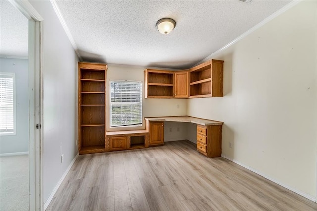 unfurnished office with a textured ceiling, baseboards, light wood finished floors, built in desk, and crown molding