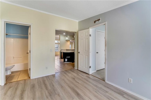 unfurnished bedroom with baseboards, light wood-type flooring, visible vents, and crown molding