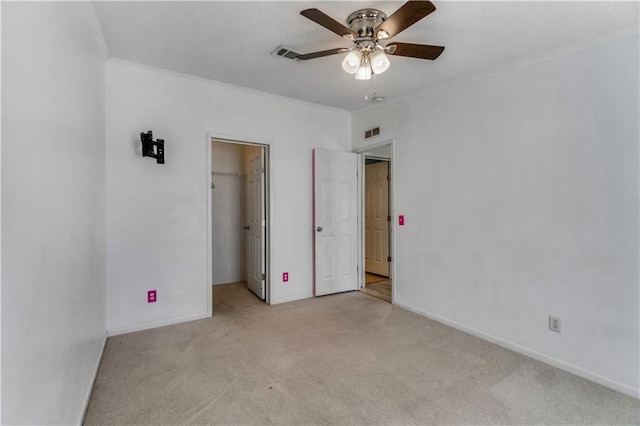 unfurnished bedroom with light carpet, a walk in closet, visible vents, and crown molding