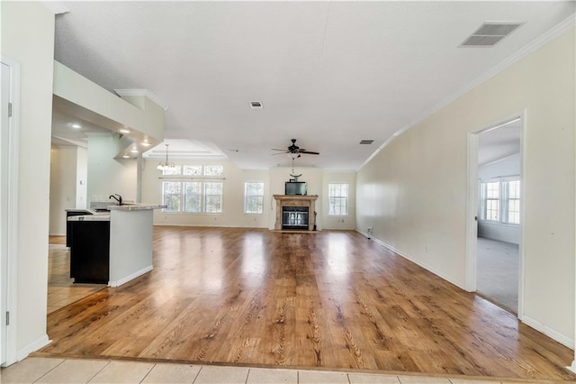 unfurnished living room featuring visible vents, a glass covered fireplace, ornamental molding, light wood-type flooring, and ceiling fan with notable chandelier