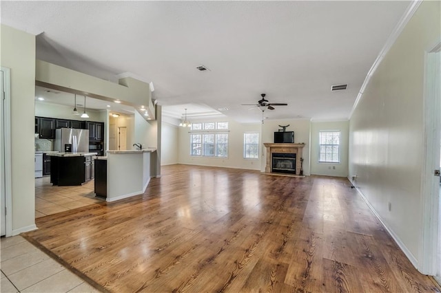 unfurnished living room with visible vents, a ceiling fan, ornamental molding, light wood finished floors, and a glass covered fireplace