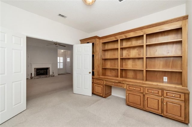 unfurnished office featuring ceiling fan, built in desk, light colored carpet, and a fireplace