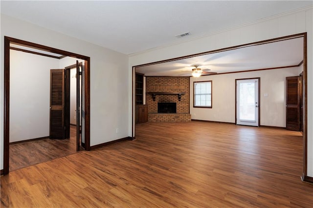 unfurnished living room featuring ornamental molding, wood-type flooring, ceiling fan, and a brick fireplace